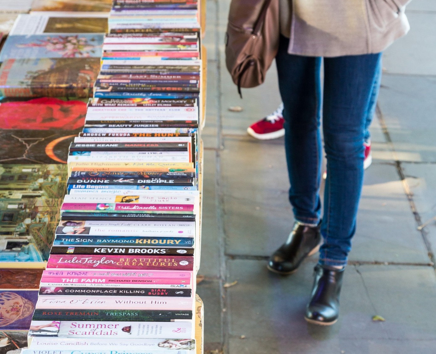 Woman looking at long table of books on footpath
