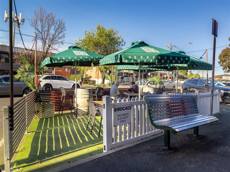 People dining outdoors at tables on a parklet with umbrellas for shade