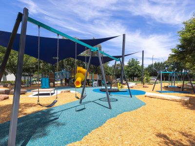 A photo of Howard Dawson Reserve's upgraded playground showing swings, shade sails, and a yellow slide on blue rubber and mulch surface